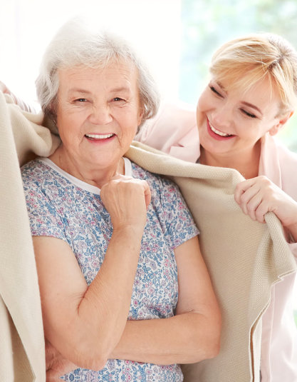 caregiver giving a blanket to senior woman while smiling