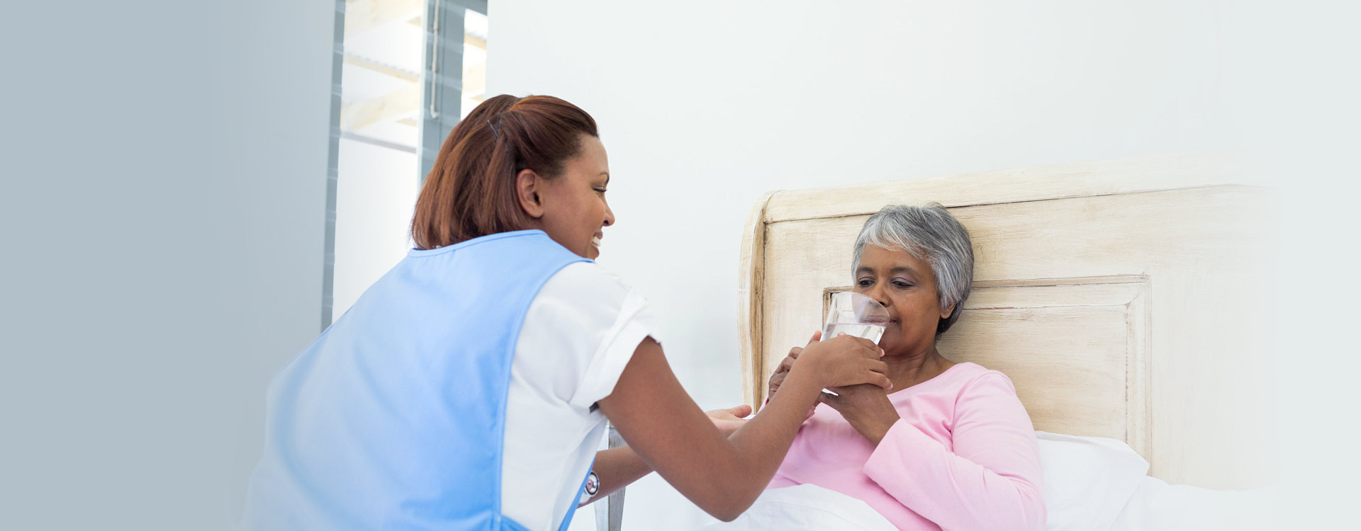 caregiver assisting the sick senior woman to drink a glass of water