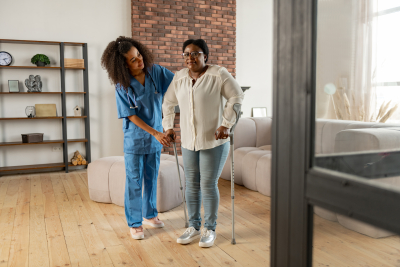 senior woman making first steps with crutches standing near private nurse