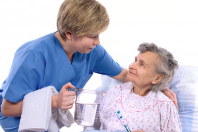 nurse holding a glass of water while helping the senior woman to brush her teeth